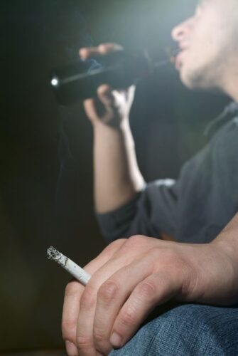 man drinking from a bottle and holding a cigarette between his fingers