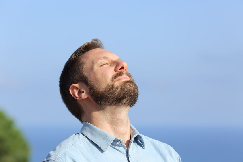 Man breathing deep fresh air outdoors with a blue sky in the background
