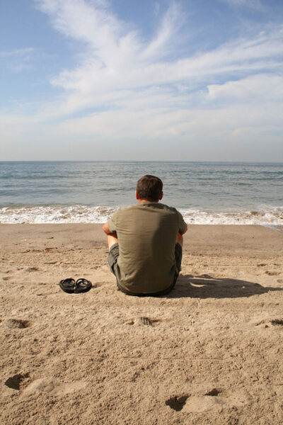 solitary man sitting on beach watching the waves